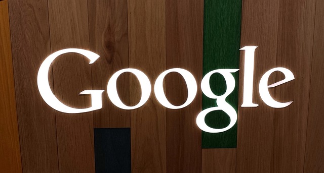 The Google logo in white, displayed on a wooden background with vertical panels of natural wood tones.