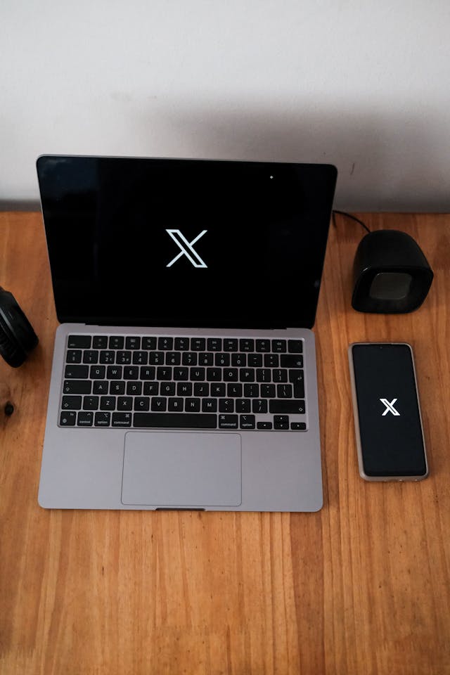 A workspace featuring a laptop and a smartphone, both displaying the same "X" logo on their screens.